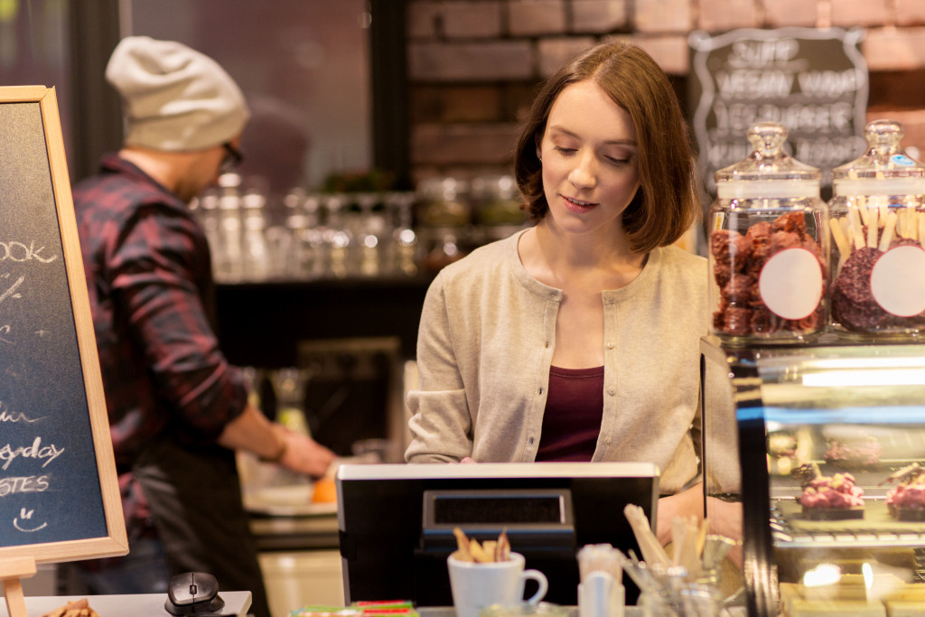 Woman or bartender at café or coffee shop counter with cashbox