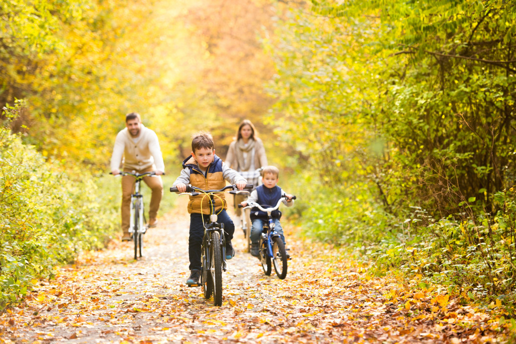 a family with two kids riding bikes in a park with autumn leaves